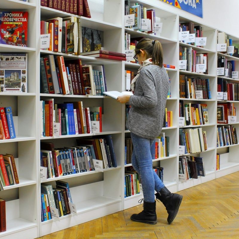 Person läuft durch eine Bibliothek mit hohen Regalen voller Bücher